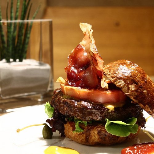 Hamburger with bacon, tomato, lettuce, and sauces on a white plate