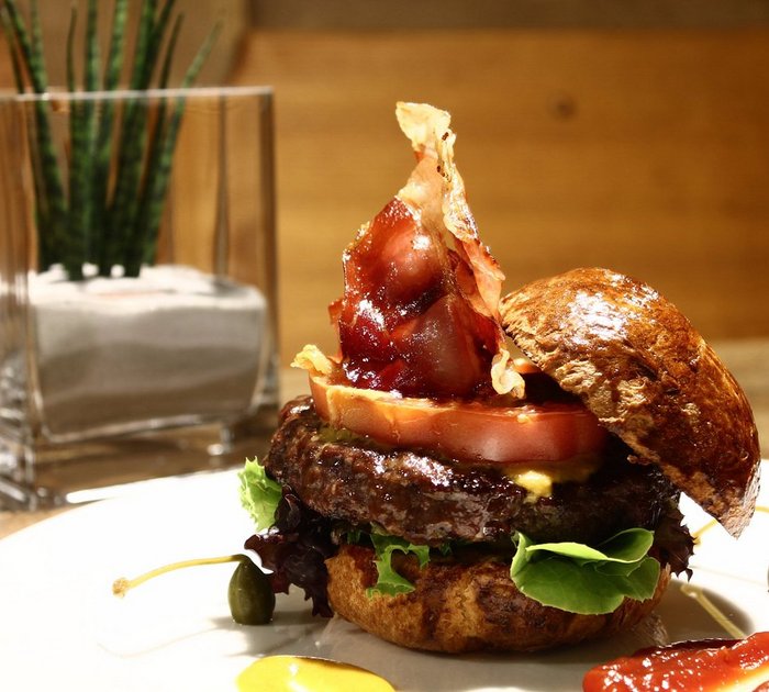 Hamburger with bacon, tomato, lettuce, and sauces on a white plate