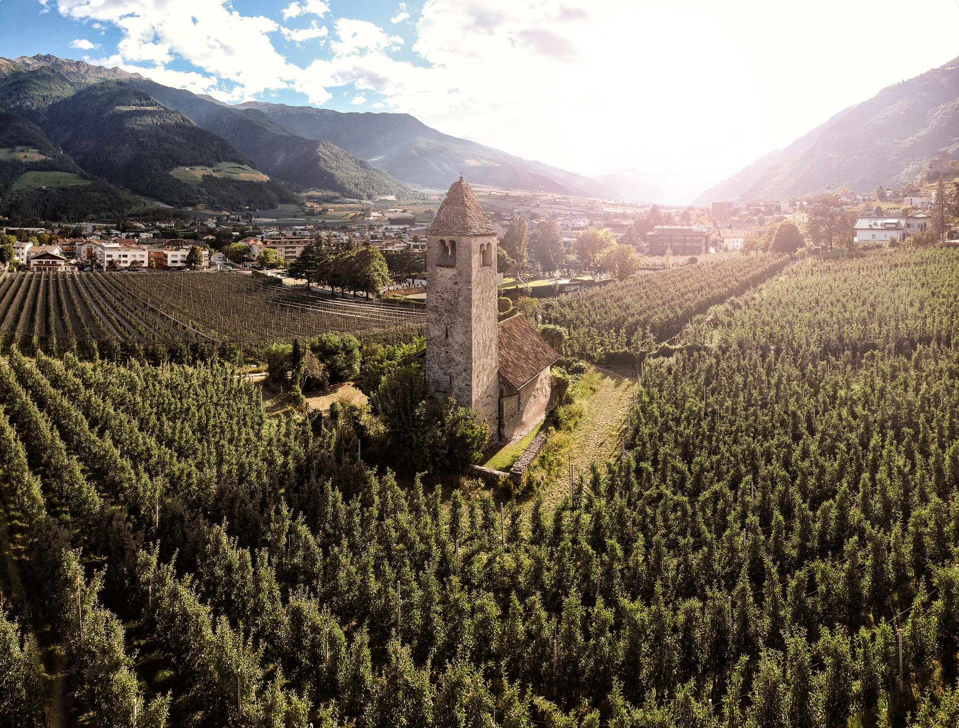 Antica torre campanaria tra frutteti di mele con montagne sullo sfondo